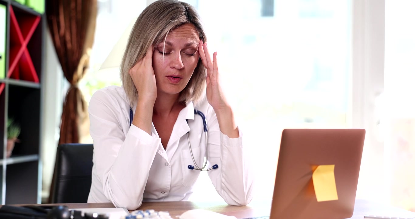Il medico siede alla scrivania premendosi le tempie, come se soffrisse di mal di testa.
