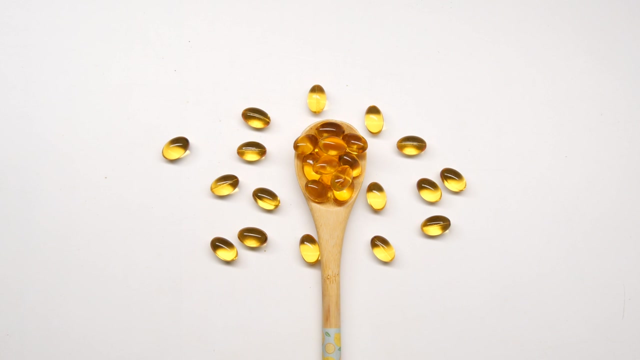 Golden Softgel Capsules in a Wooden Spoon on White Background