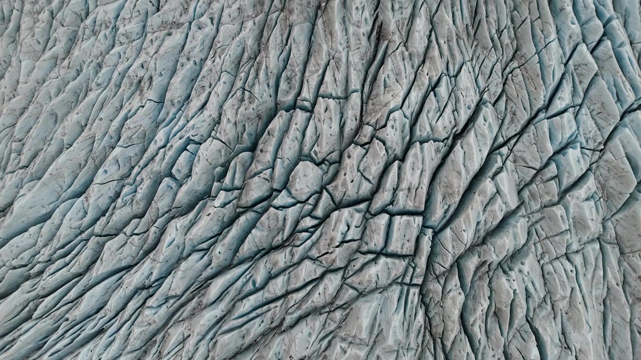 Riprese cinematografiche con drone che sorvolano profondi crepacci su un enorme ghiacciaio islandese, con guide glaciali che camminano attentamente sulla superficie ghiacciata. Prospettiva aerea drammatica che mostra la vastità.