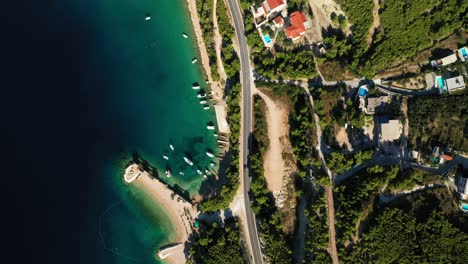aerial drone footage of cars driving through a village on a coastal road
