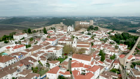 Vista-Panorámica-De-Casas-Blancas,-Techos-De-Tejas-Rojas-Y-Castillo-Desde-La-Muralla-De-La-Fortaleza-En-El-Pueblo-De-Obidos,-Portugal---Toma-Aérea-De-Drones