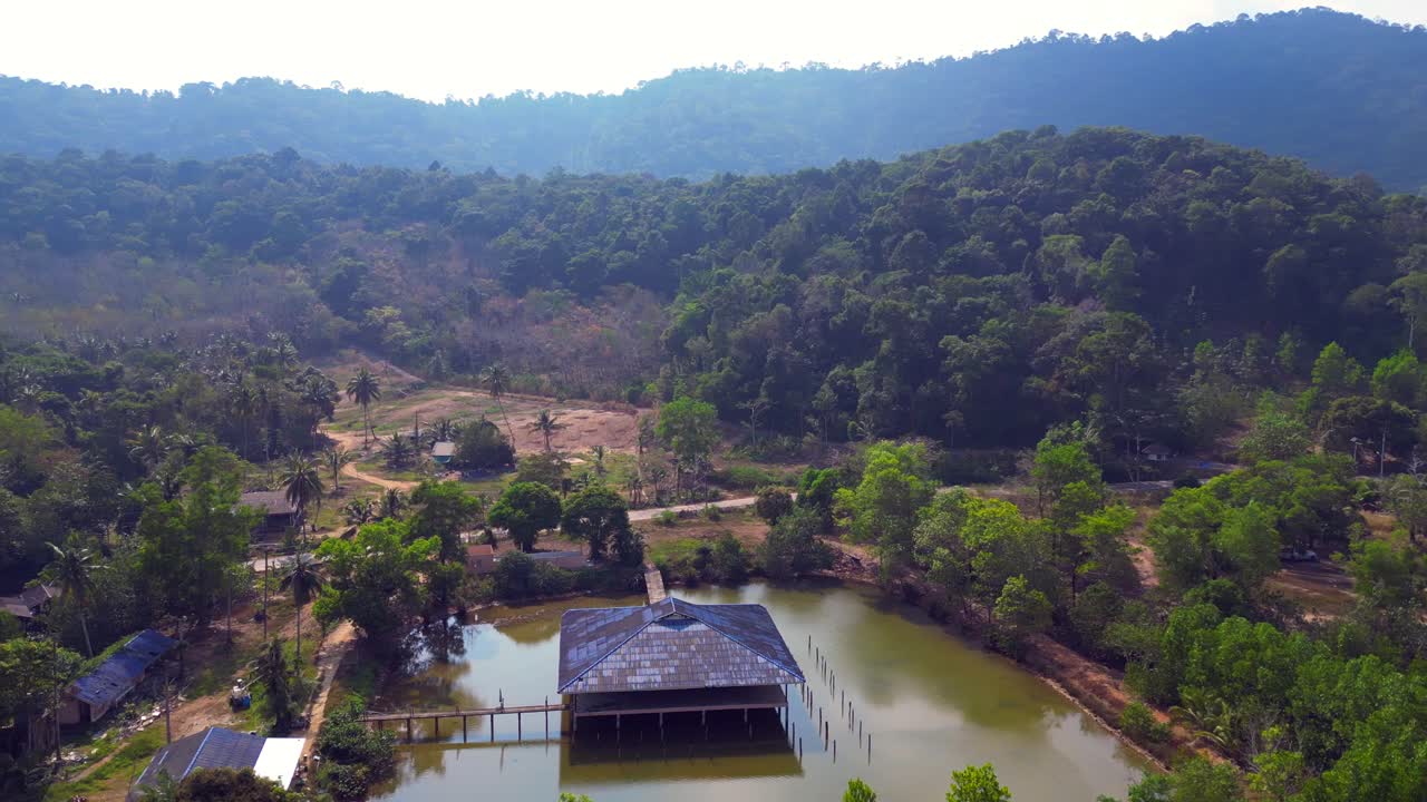 Dense mangrove forest and a building on stilts in a pond on Koh Chang Trat bay Thailand. Best aerial view rotation pan to left drone