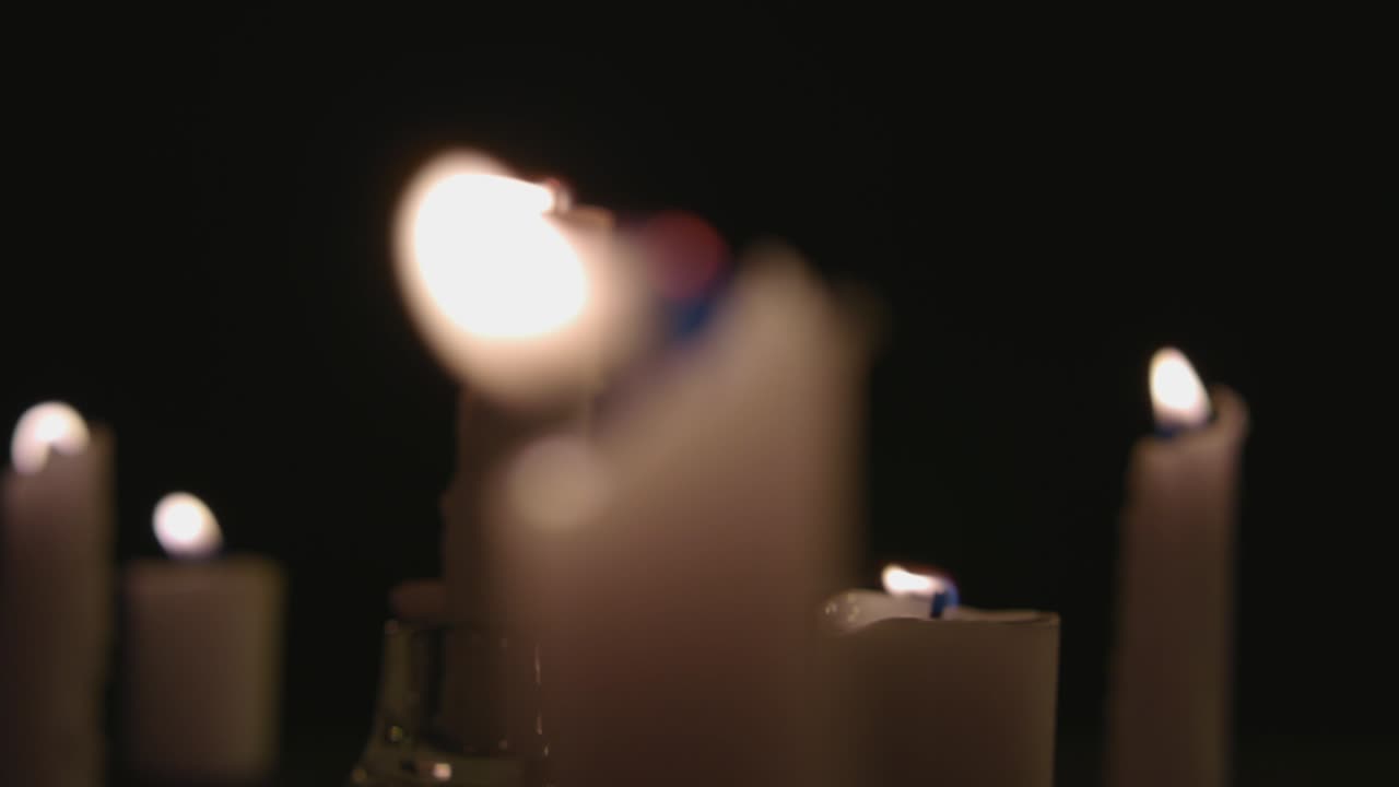 Un primissimo piano e una panoramica di candele bianche accese con uno sfondo nero