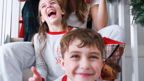 portrait of excited family wearing pajamas sitting on stairs on christmas morning