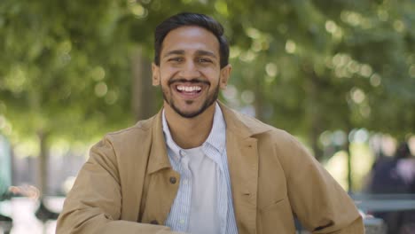 Porträt-Eines-Lächelnden-Muslimischen-Mannes,-Der-Am-Tisch-Im-Freien-Auf-Der-Stadtstraße-Sitzt