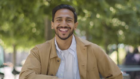 portrait of smiling muslim man sitting at outdoor table on city street