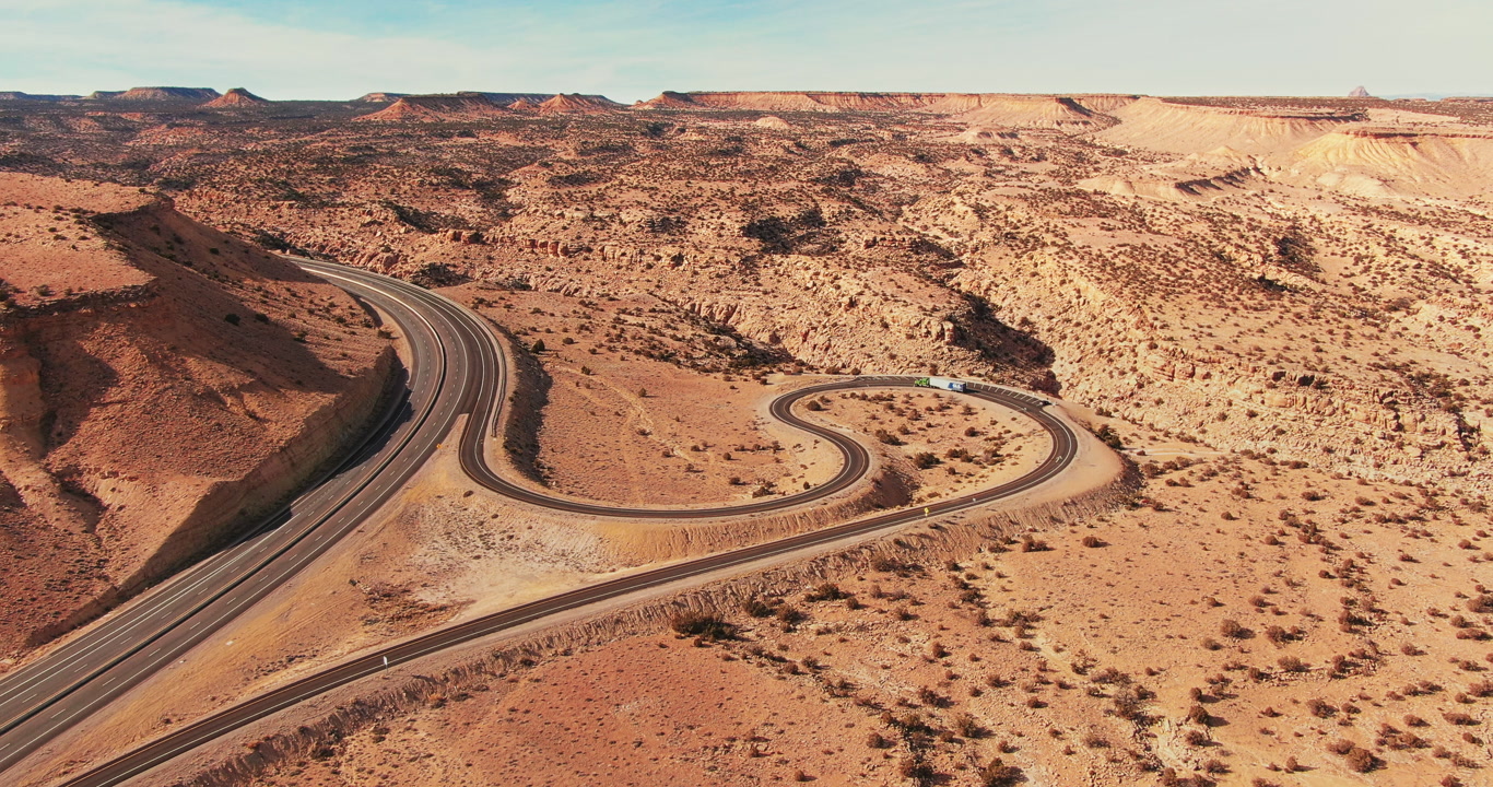 Aerial view of a winding highway cutting through the arid desert landscape of Utah. The road curves gracefully amidst the rugged terrain. Smooth panning camera movement
