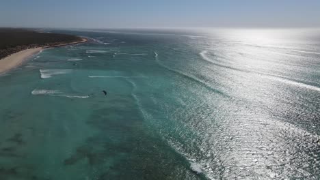 sobrevuelo aéreo océano cristalino con kite surf divirtiéndose durante el día ventoso y soleado en australia