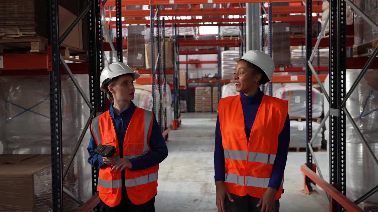 Two Female Warehouse Workers Walking and Talking in Distribution Center