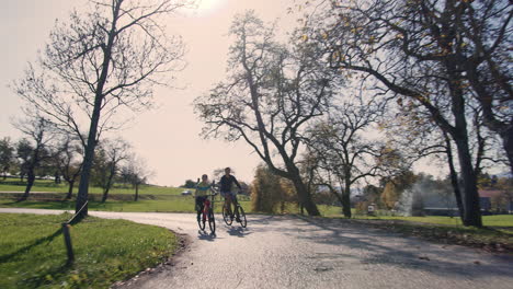 Pareja-De-Ciclistas-Chocando-Los-Cinco-Mientras-Viajan-Por-El-Campo,-Plano-Amplio