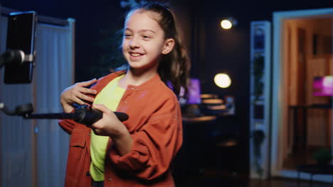 Una-Niña-Graciosa-Grabando-Un-Video-De-Baile-Moderno-Para-Las-Redes-Sociales-Usando-Un-Teléfono-Celular-Conectado-A-Un-Palo-Selfie