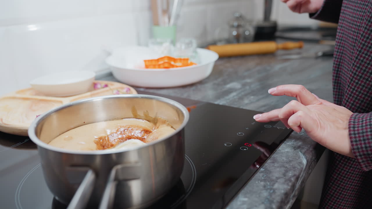 primer plano de la cocción de alimentos en la estufa eléctrica con varios utensilios de cocina cerca mientras la persona ajusta la temperatura al nivel cinco, panel de control táctil moderno y encimera elegante