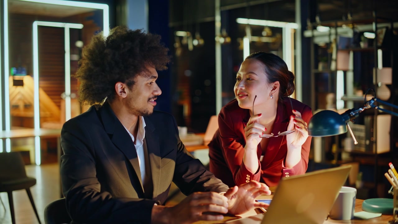 Woman playfully removing glasses from colleague. Office flirting night desk.