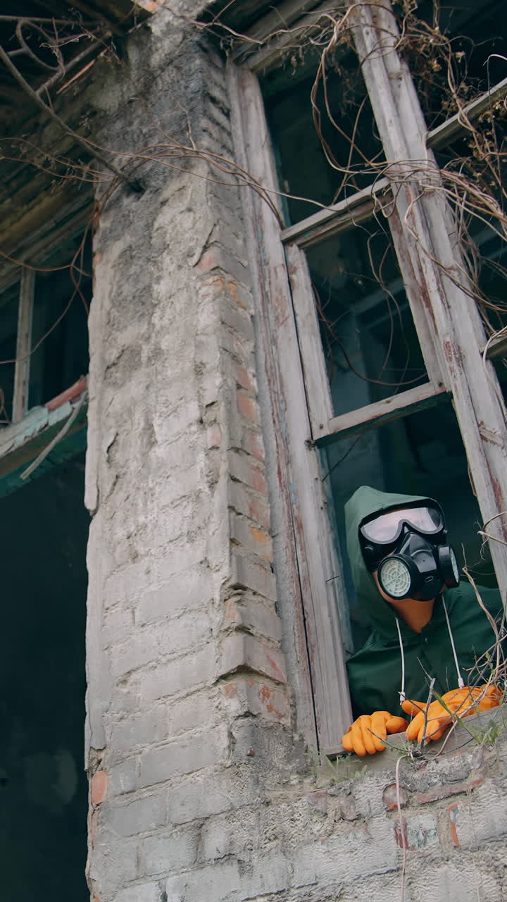 Human in respirator looking from ruined building with broken windows. Flower pot and ecologist in the abandoned place after biological attack. Vertical video