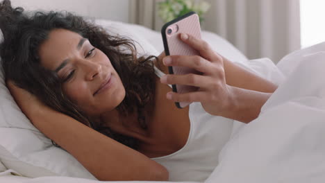 mujer feliz usando un teléfono inteligente en la cama enviando mensajes de texto compartiendo mensajes en las redes sociales disfrutando de la conexión en línea relajándose en casa