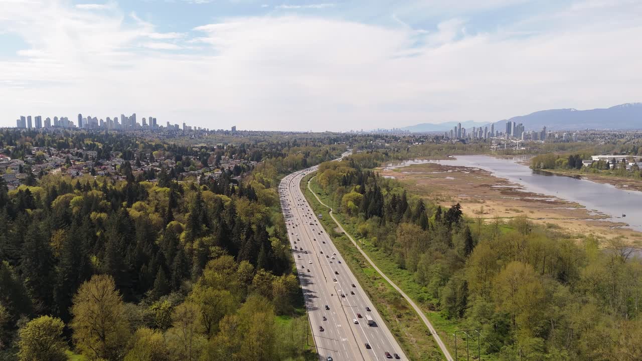 Aerial View Captures Highway Traffic Amidst Lush Forests and City Skyline in British Columbia