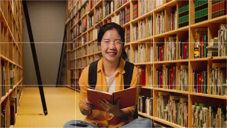 pantalla tomó la foto de una estudiante asiática con una mochila leyendo un libro y luego sonriendo a la cámara mientras estaba de pie en la biblioteca
