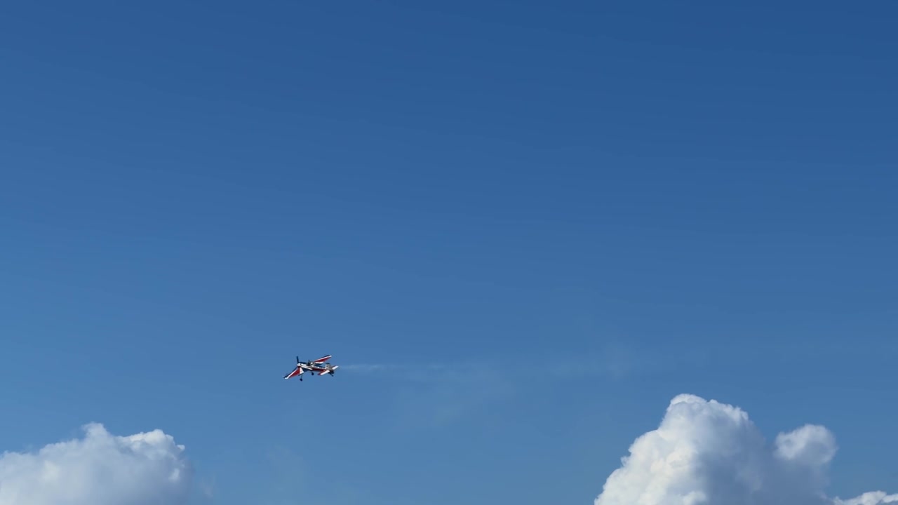 Un aereo acrobatico rosso esegue manovre acrobatiche con scie di fumo contro un cielo blu