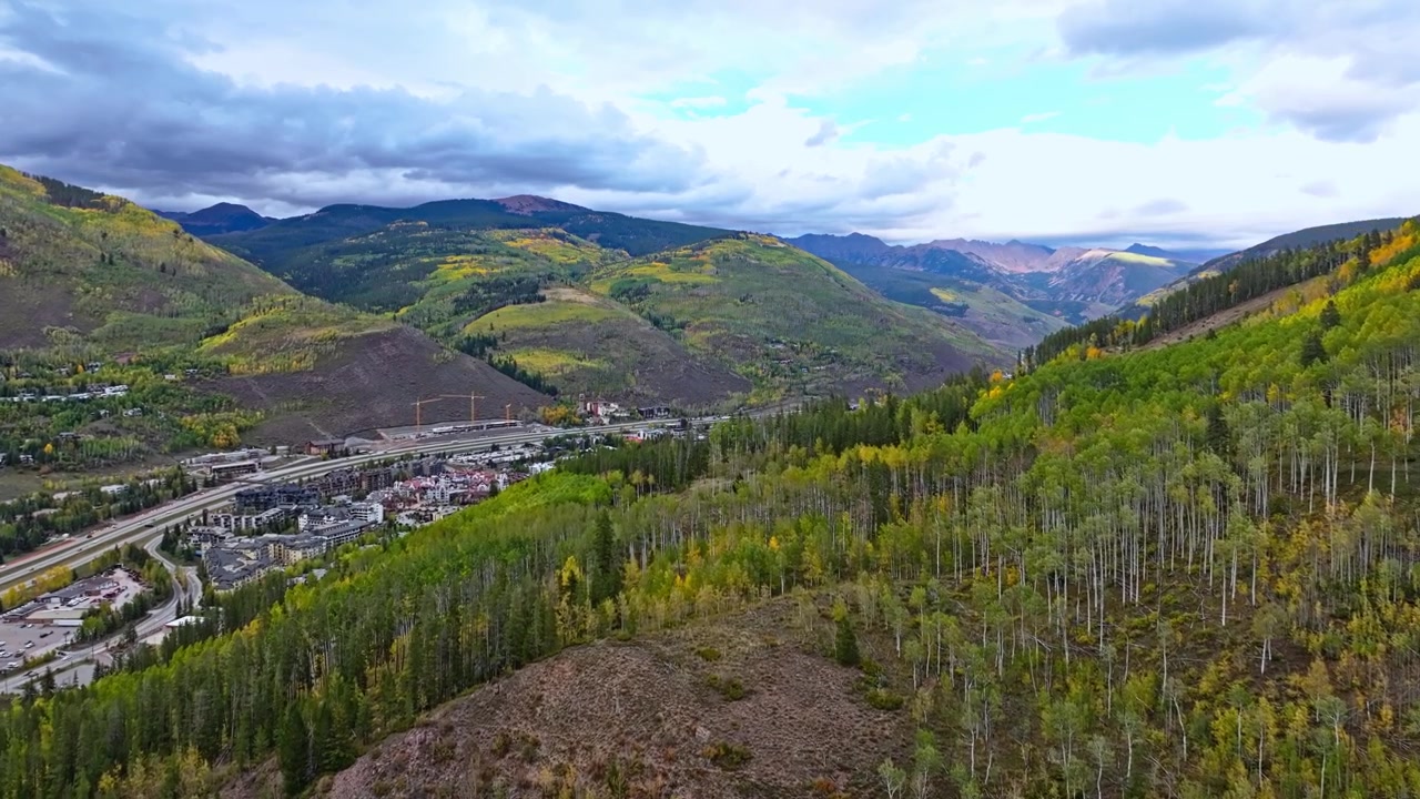 Boschi radi e fogliame autunnale giallo coprono i pendii ondulati sotto le nuvole a Vail, Colorado, ripresa aerea panoramica con dolly ascendente, stagione autunnale a Vail, Colorado