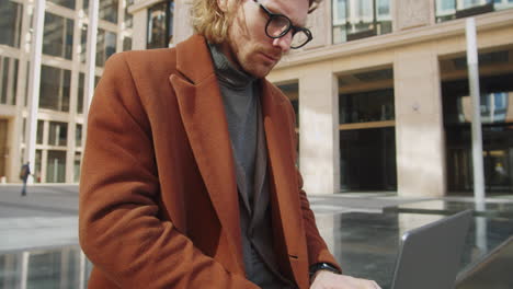 joven hombre de negocios guapo trabajando en una computadora portátil al aire libre en el centro de la ciudad