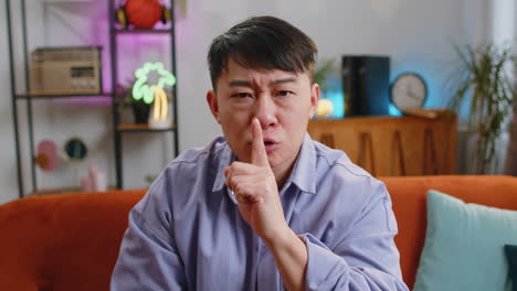 asian man presses finger to lips makes silence hush sign do not tells gossip secret, quiet at home