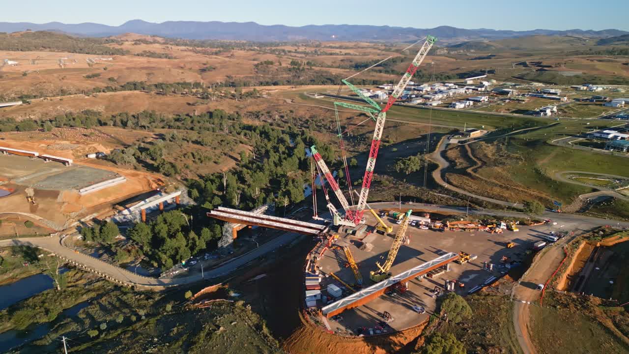 Drone captures the Molonglo bridge project in Canberra with a large crane lifting steel beams over the river below.