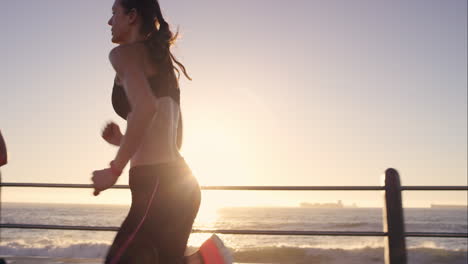 dos mujeres atléticas corriendo al aire libre en cámara lenta en el paseo marítimo al atardecer cerca del océano disfrutando de la carrera nocturna