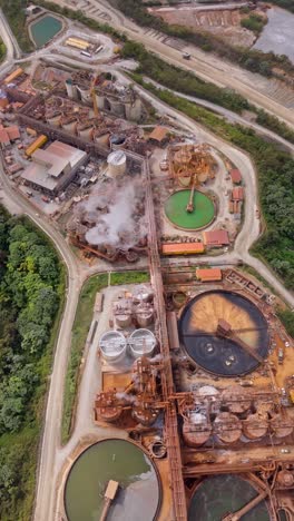 vertical aerial drone shot of large gold mining industrial complex with processing tanks, buildings, and smoke, showcasing resource extraction. suitable for industrial or environmental themes