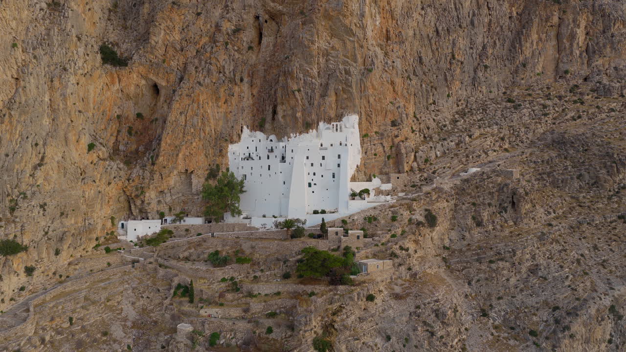 Aerial pullback shot reveals Holy Monastery of the Virgin Mary Chozoviotissa on steep cliffside at sunrise, The Panagia Hozoviotissa Monastery, Amorgos Island, Drone shot