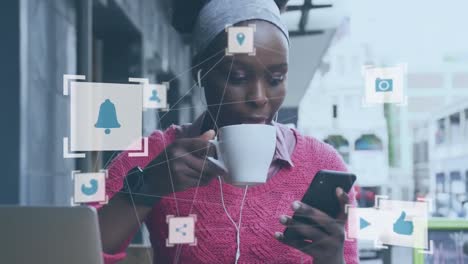 Animation-of-media-icon-network-over-happy-african-american-woman-using-smartphone-at-street-cafe