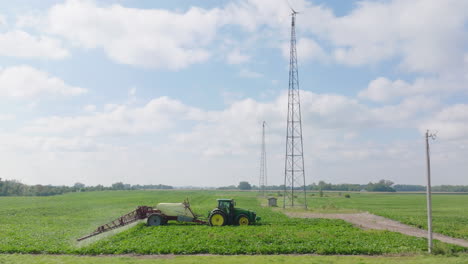 vista lateral aérea de un tractor con pulverizador de brazo rociando pesticidas en cultivos frescos