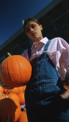 woman holding pumpkin in pink shirt and denim overalls