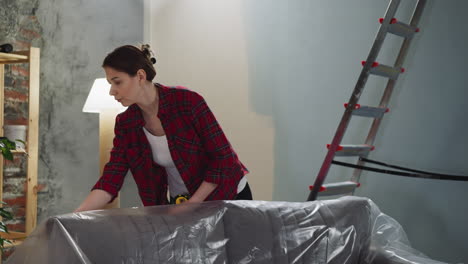 la mujer cubre el sofá con papel de aluminio para protegerlo de las gotas de pintura