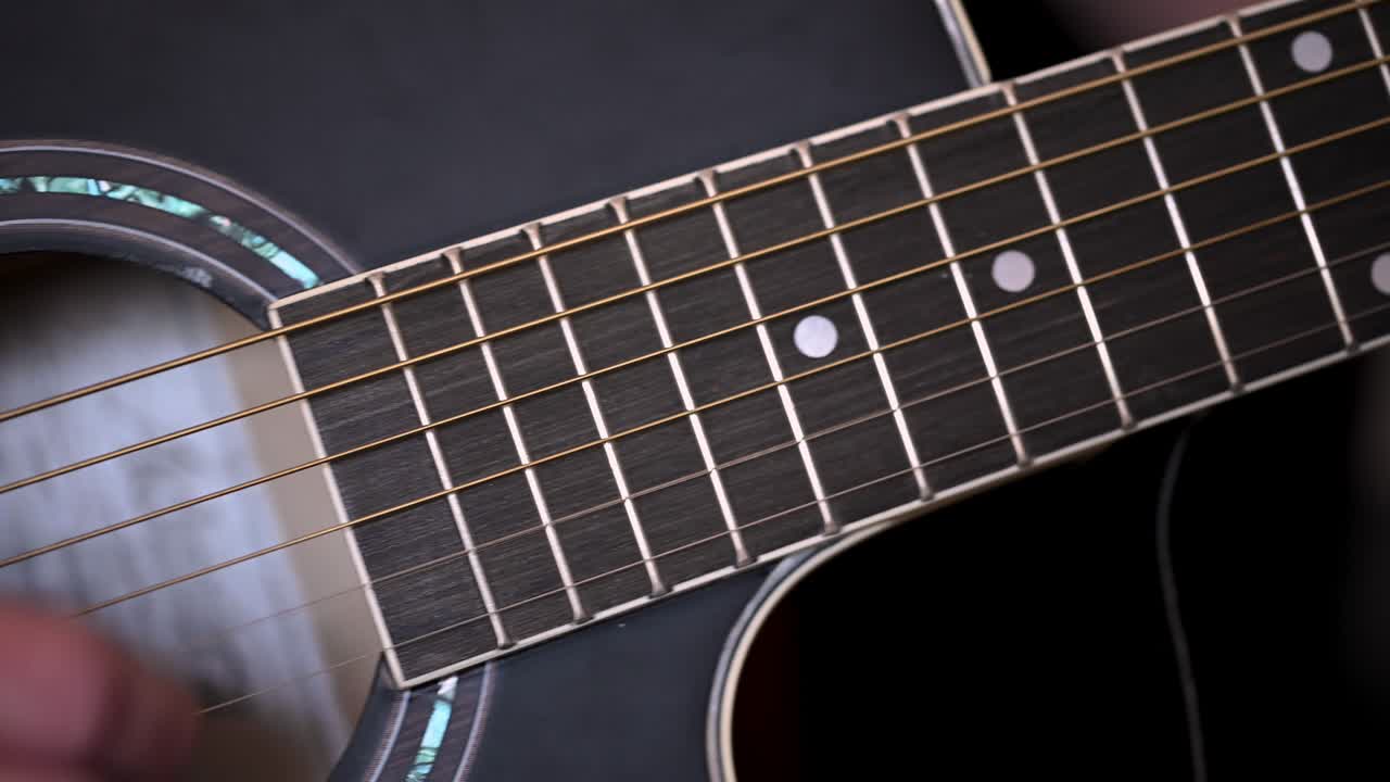 la mano del hombre poniendo acordes en los trastes del mástil de una guitarra acústica negra a la otra mano tocando las cuerdas