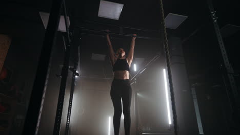 a sporty young woman pulls herself up on a horizontal bar in a dark gym in a beautiful neon backlight. endurance and perseverance in pulling up movement towards the goal