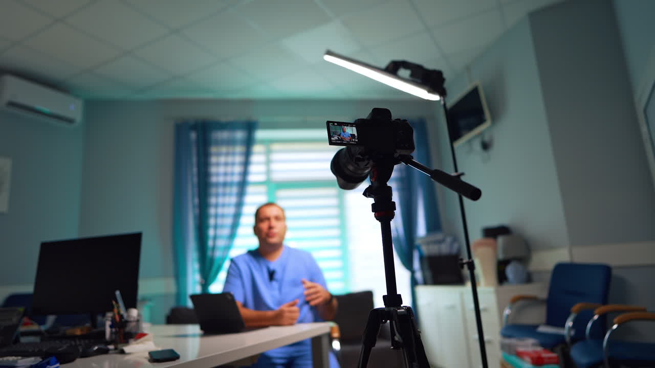 Confident male doctor in blue uniform recording a video for his vlog. Camera on tripod taking video of a man. Low angle view. Selective focus