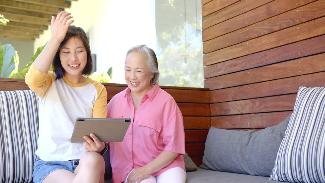 Smiling senior asian woman and young asian woman using tablet together on outdoor patio