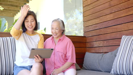 smiling senior asian woman and young asian woman using tablet together on outdoor patio