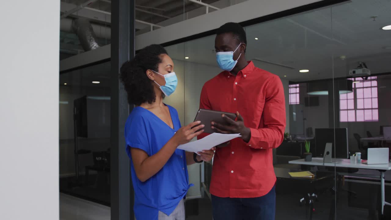 Diverse race male and female business colleagues wearing face masks discussing over tablet