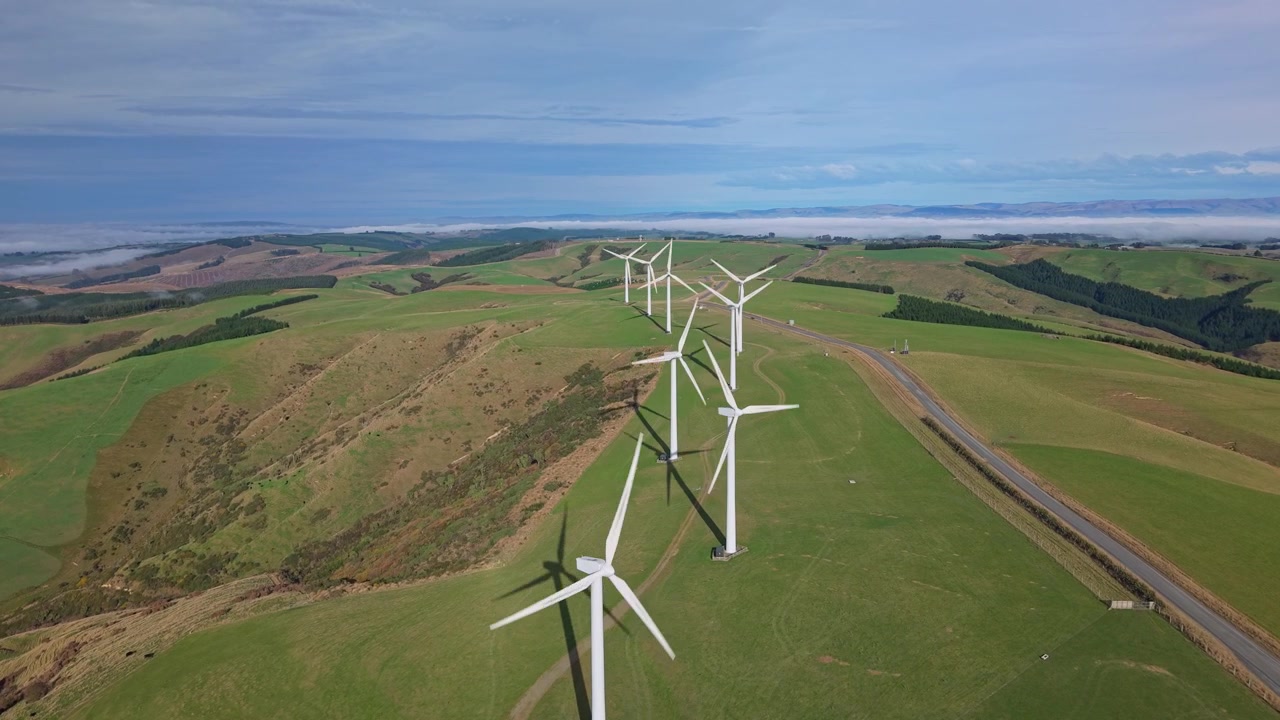 Aerial drone footage of a wind farm in Central Otago, New Zealand, featuring modern wind turbines, rolling green hills, and clean renewable energy in a scenic rural landscape.