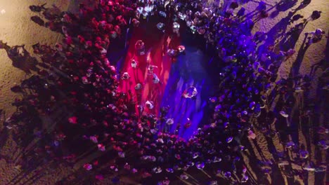 rising aerial looking straight down at a dance floor on an outdoor beach at night during a rave on the caribbean island of st kitts