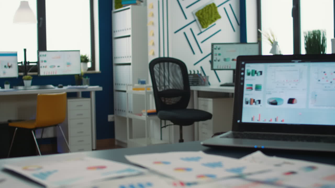 Empty startup office with multiple computer screens displaying financial statistics and closeup on laptop