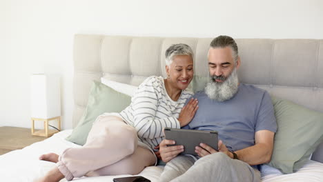 relaxing on bed, senior couple smiling and using tablet together