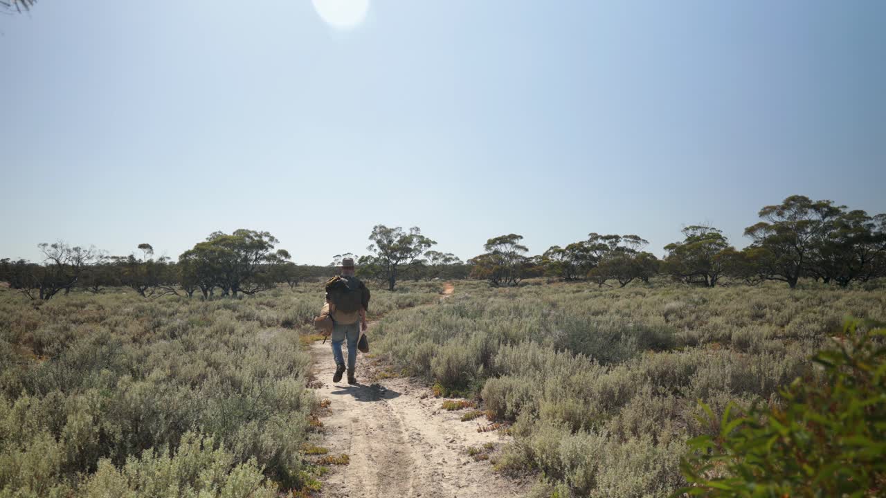 un swagman camina por un sendero del desierto a través del interior de australia