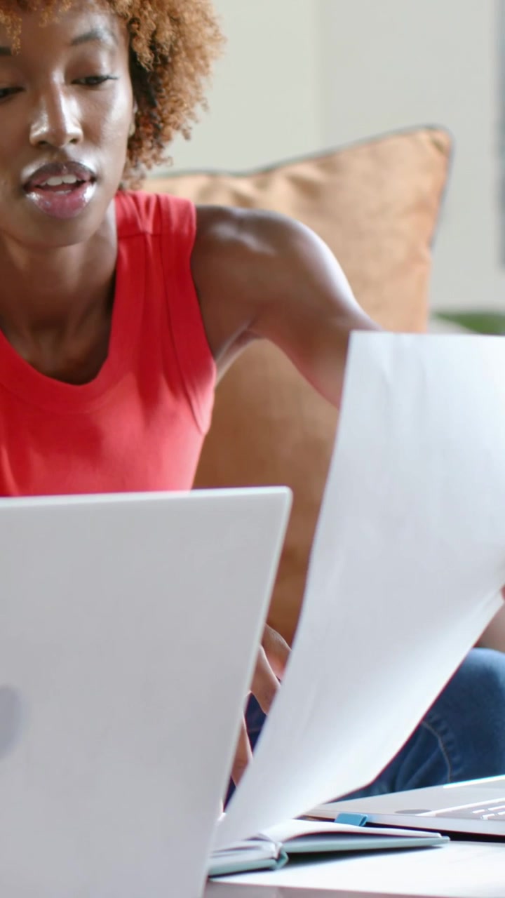 Video verticale: Donna appoggiata con top rosso senza maniche che controlla pagine con il laptop sul divano per lavoro.
