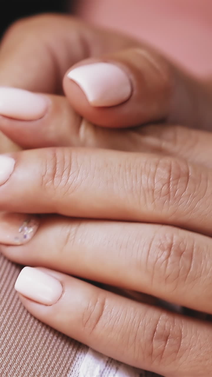 CU, slow motion: young woman wearing white transparent stockings holds hands with elegant beige manicure and glitter on blurred background closeup