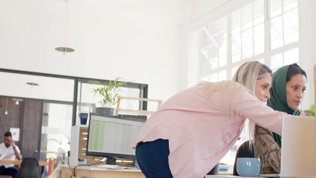 Indaffarate e diverse donne d'affari che discutono di lavoro con laptop in ufficio al rallentatore