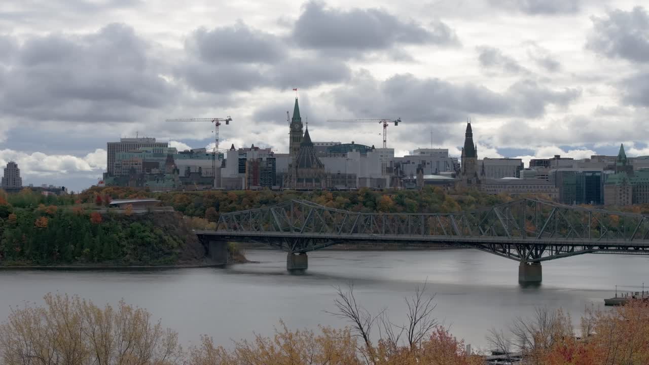Views of Parliament Hill with Alexandra Bridge and Ottawa River in foreground in the fall on a cloudy day in Ottawa Ontario Canada