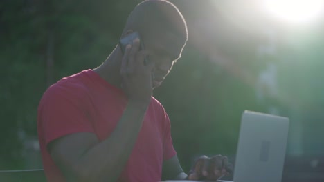 young afro-american man typing on laptop, talking on phone