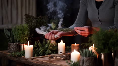 a person performing a spiritual smudging ritual with burning sage, candles, and plants